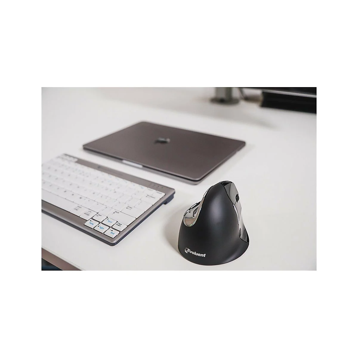 Draufsicht auf eine Tastatur, einen Laptop und eine ergonomische Maus auf einer weißen Oberfläche. Der Maus steht im Fokus.