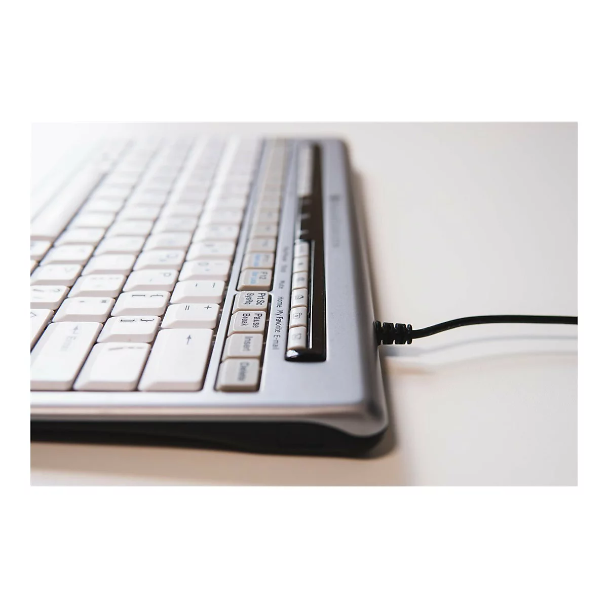 Nahaufnahme einer Computertastatur mit silbernem Gehäuse, weißen Tasten und einem schwarzen Kabel.