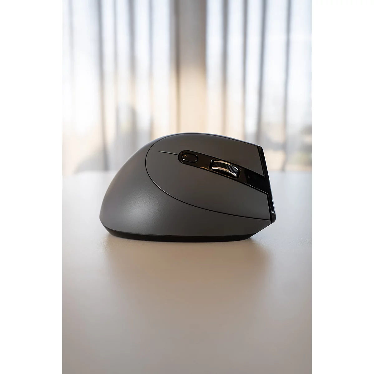 Graue ergonomische Maus auf weißem Tisch. Fenster im Hintergrund.