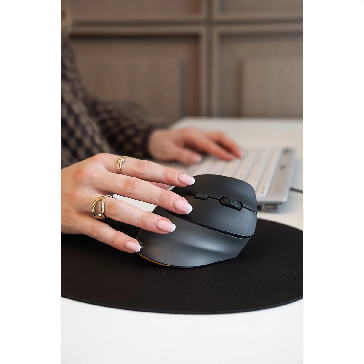 Hand bedient eine ergonomische schwarze Vertikalmaus auf einem runden schwarzen Mauspad.