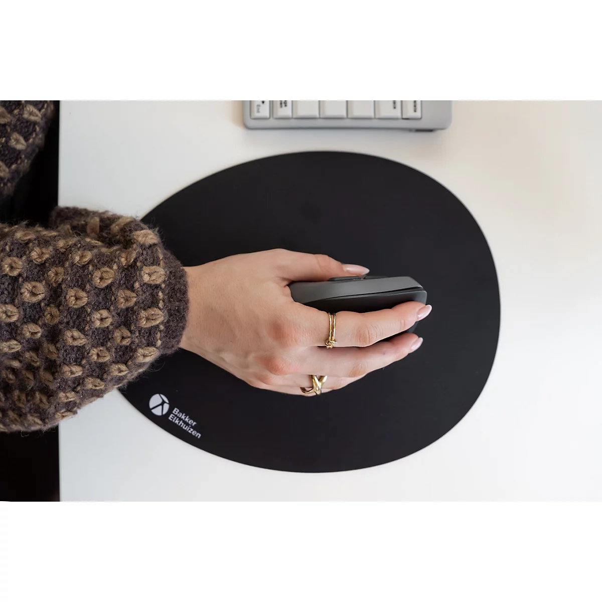 Draufsicht einer Hand mit Ringen, die eine ergonomische Maus auf einem schwarzen, runden Mauspad bedient.