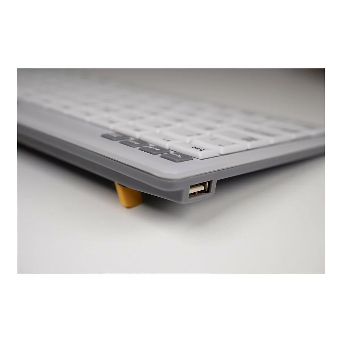 Nahaufnahme der Seite einer grauen Tastatur mit einem gut sichtbaren USB-Anschluss und einem gelben Ständer.