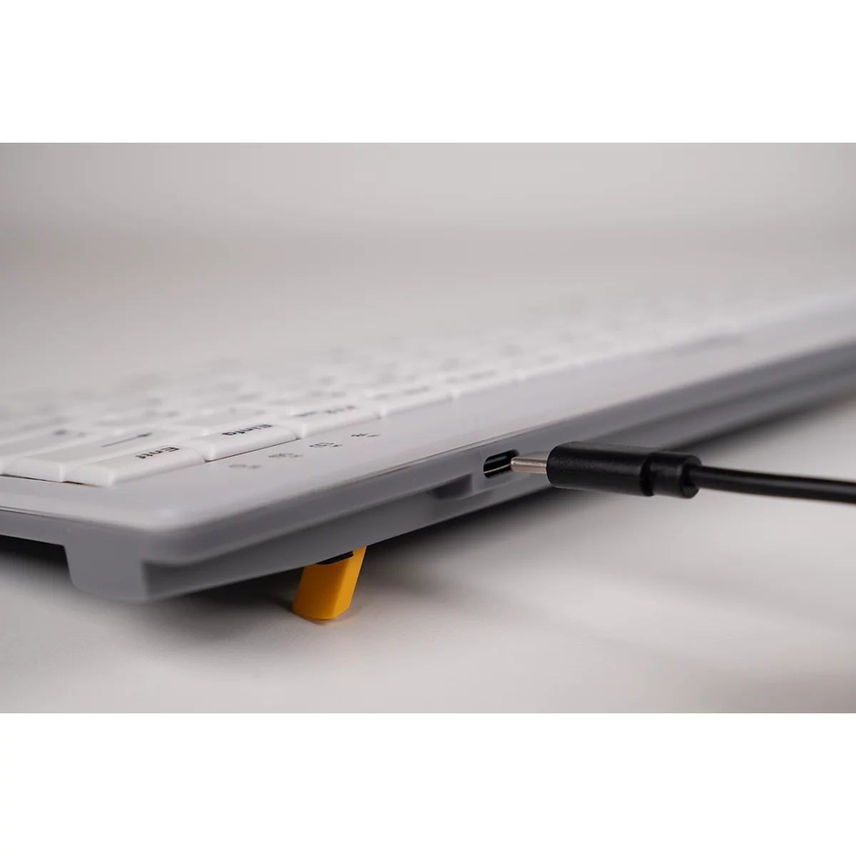 Nahaufnahme einer Tastatur mit angeschlossenem USB-C-Kabel. Gelber Fuß hebt Tastatur an, Detail der Tasten.