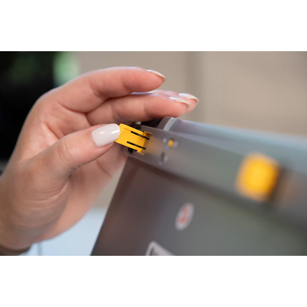 Nahaufnahme einer Hand, die einen gelben Stecker in ein graues Gerät einsteckt.
