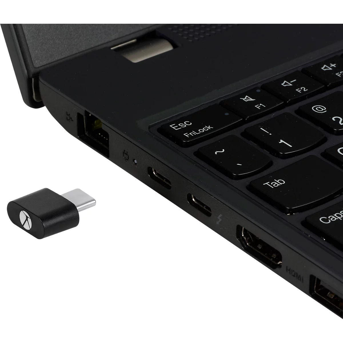 Schwarzer USB-C-Adapter neben einem Laptop. Der Adapter ist im Detail zu sehen, die Tastatur ist teilweise im Bild.