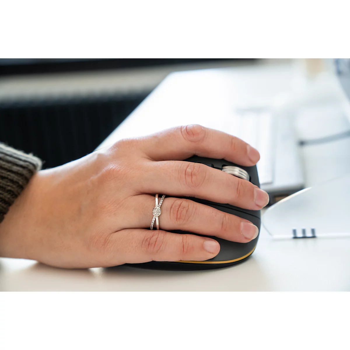 Hand mit Ring auf ergonomischer Maus. Der Ring hat einen Diamanten.