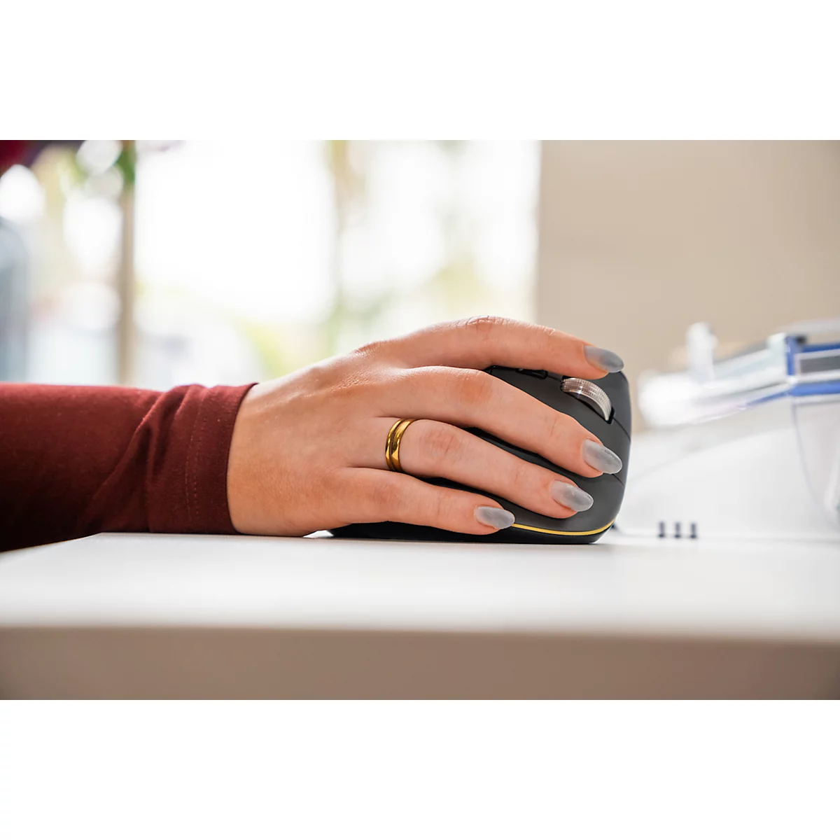 Hand einer Frau auf einer Computermaus, lackierte Nägel, goldener Ring, bordeauxfarbener Ärmel.