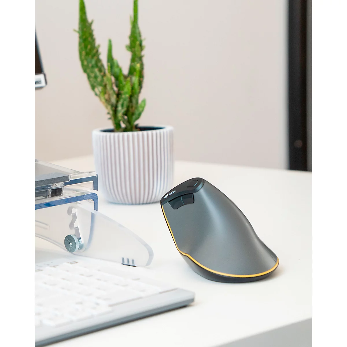 Ergonomische Maus auf weißem Tisch mit Topfpflanze und Tastatur im Hintergrund.