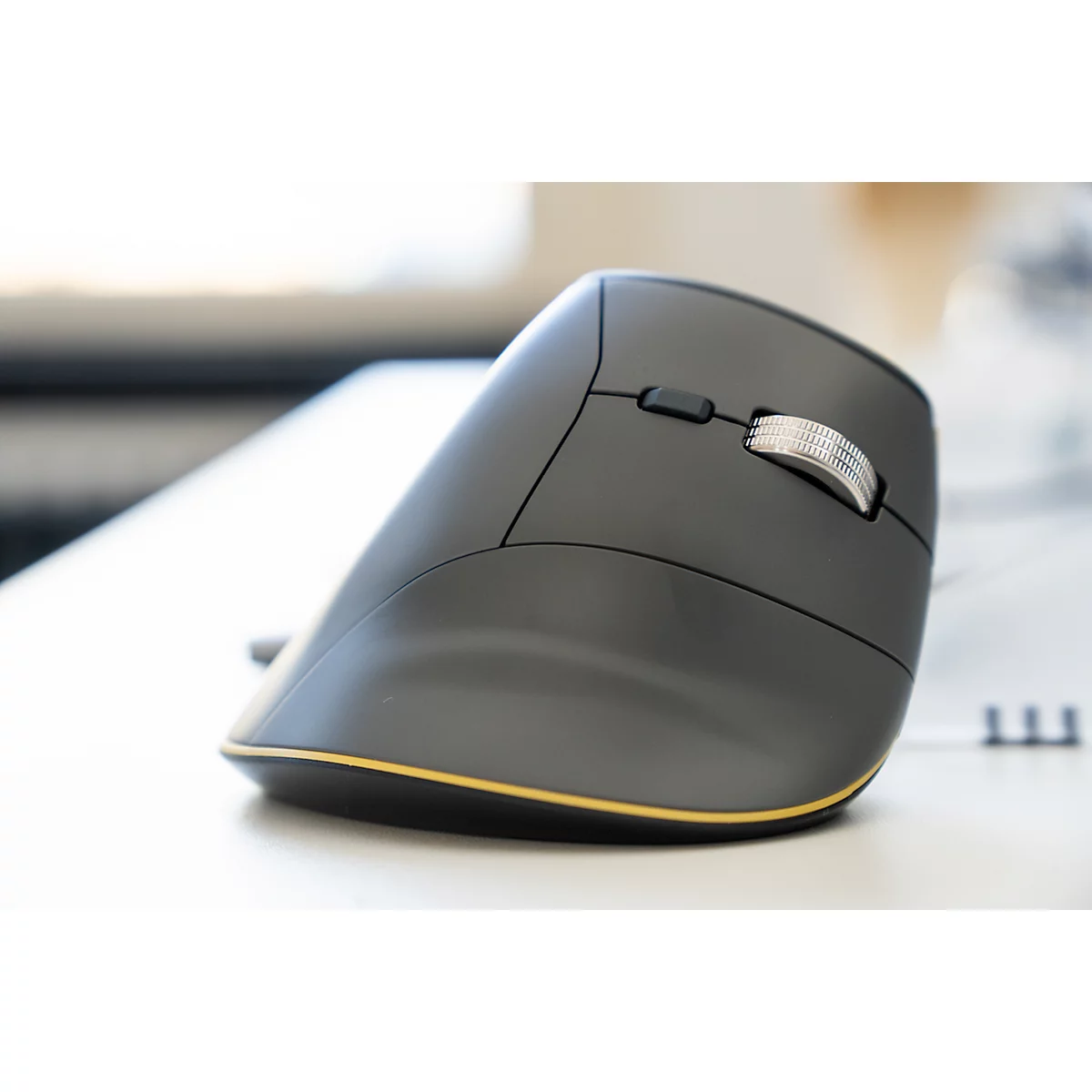 Ergonomische graue Maus, Detailaufnahme. Goldfarbener Rand, silbernes Scrollrad, liegt auf weißem Tisch.