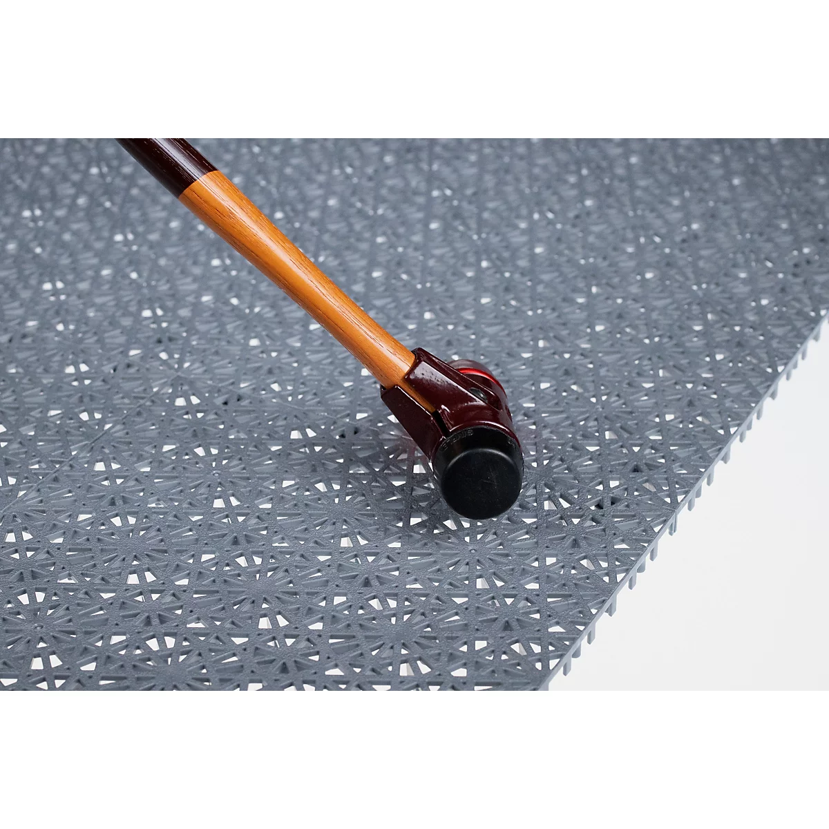 Primer plano del pie de un bastón apoyado sobre una alfombrilla de suelo gris y texturizada.