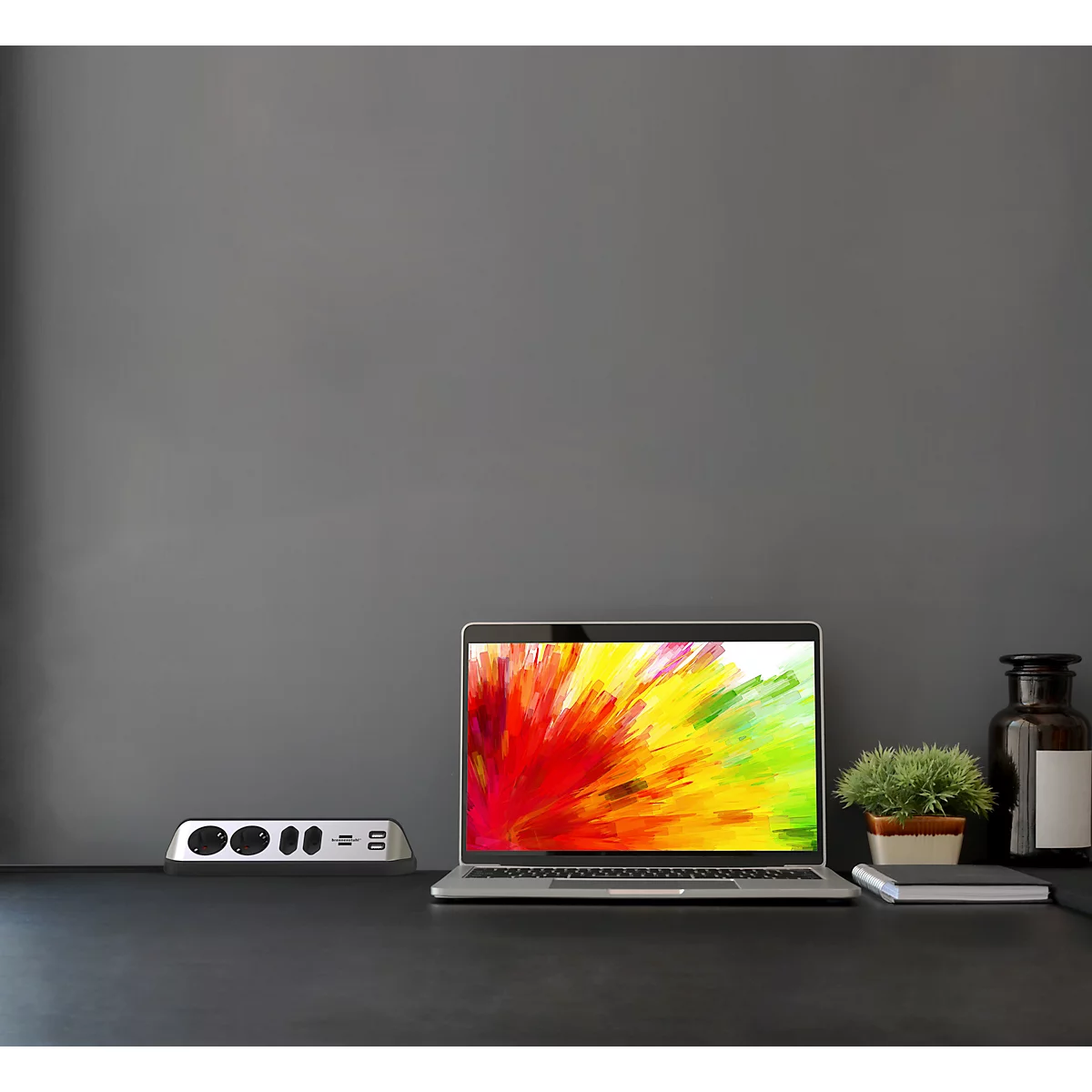 Ordinateur portable avec écran coloré, accessoires et décoration sur une table sombre. Fond gris.
