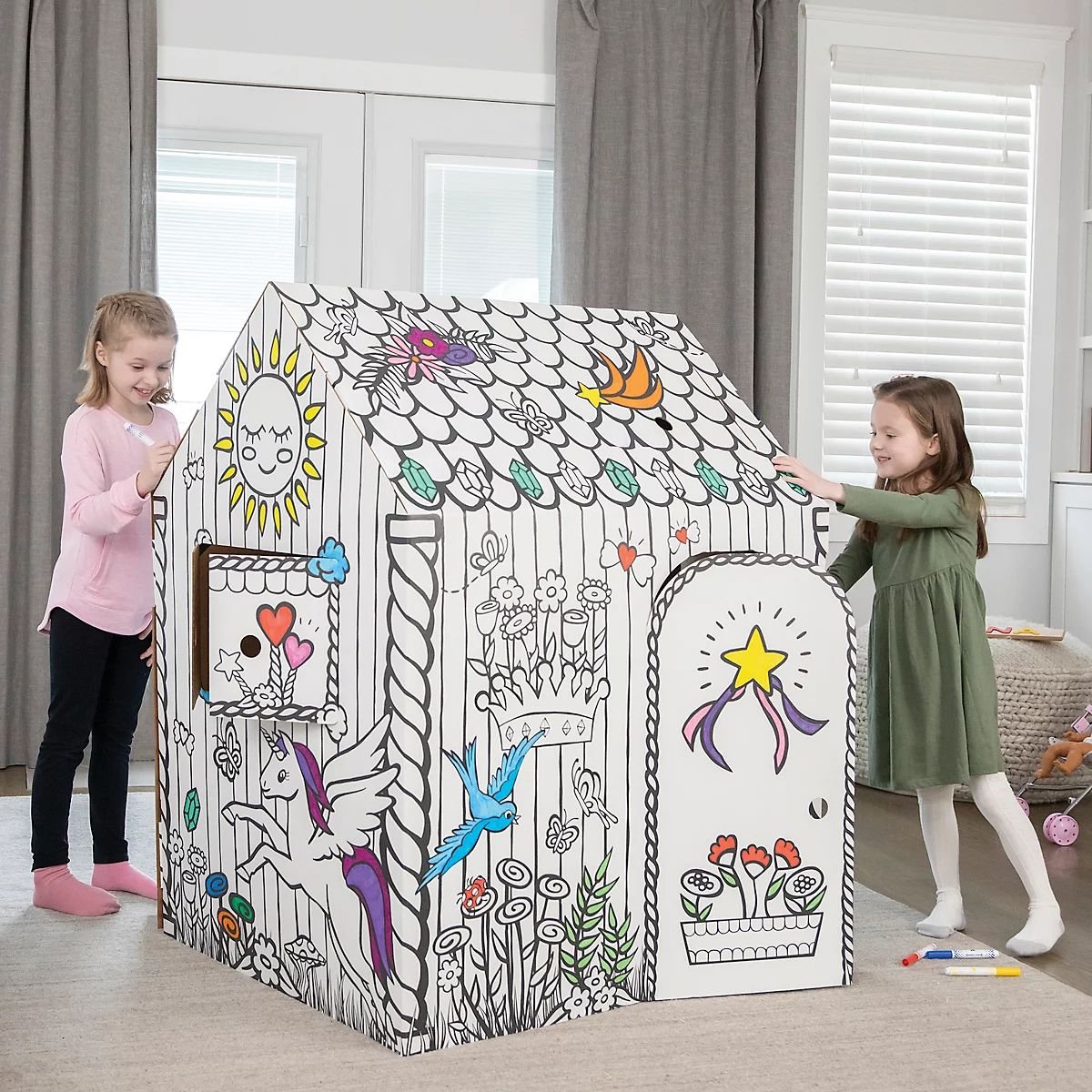 Deux filles jouent dans une maison de coloriage, décorée d'images colorées. L'une dessine, l'autre tient la porte.