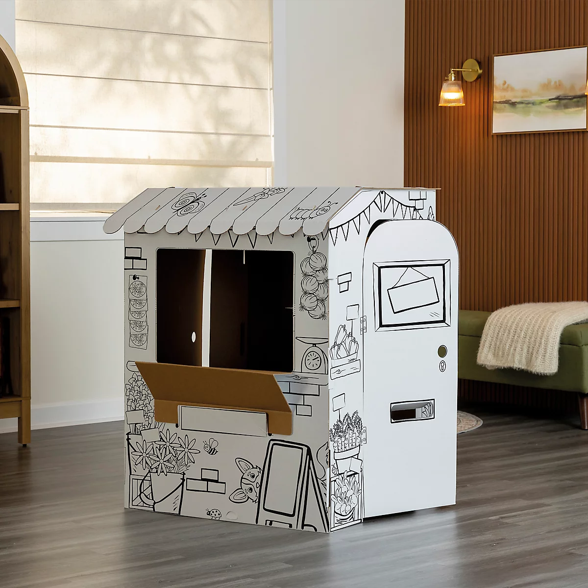 Ein Marktstand aus Pappe, bemalt mit Umrissen von Produkten und Schildern, steht in einem Zimmer.