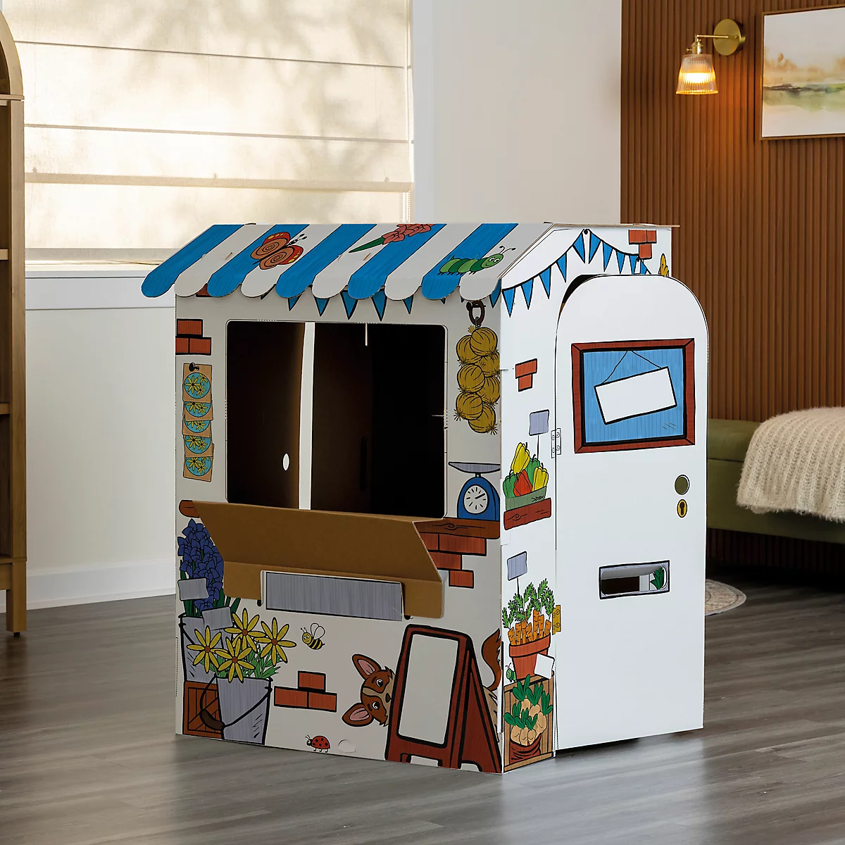 Ein Marktstand aus Pappe, mit blau-weiß gestreiftem Dach und bemalten Details: Früchte, Gemüse, Blumen, Preisliste, und Preisschild.