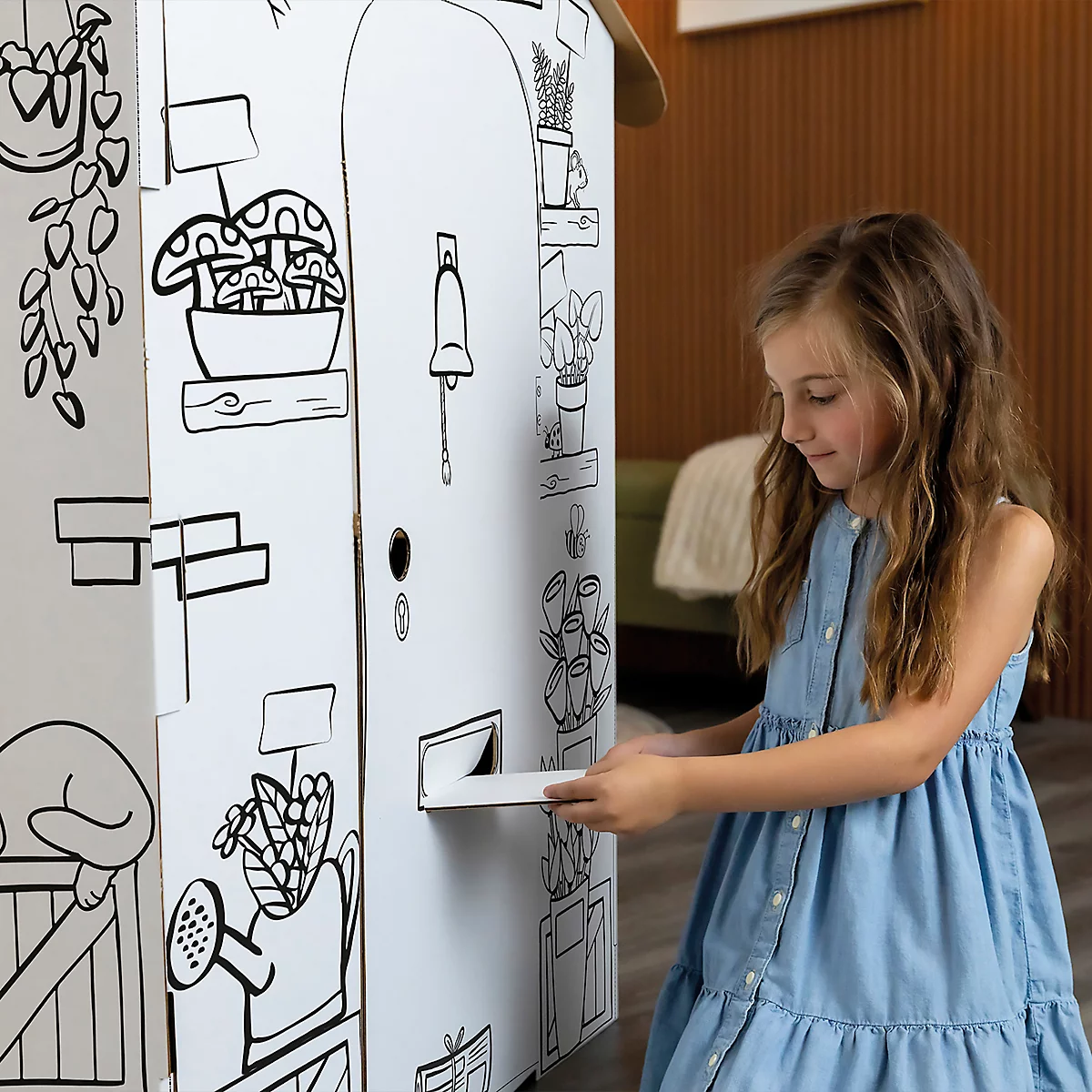 Ein Mädchen mit langem Haar öffnet einen Briefkasten an einem weißen Spielhaus, das mit schwarz umrandeten Illustrationen verziert ist.