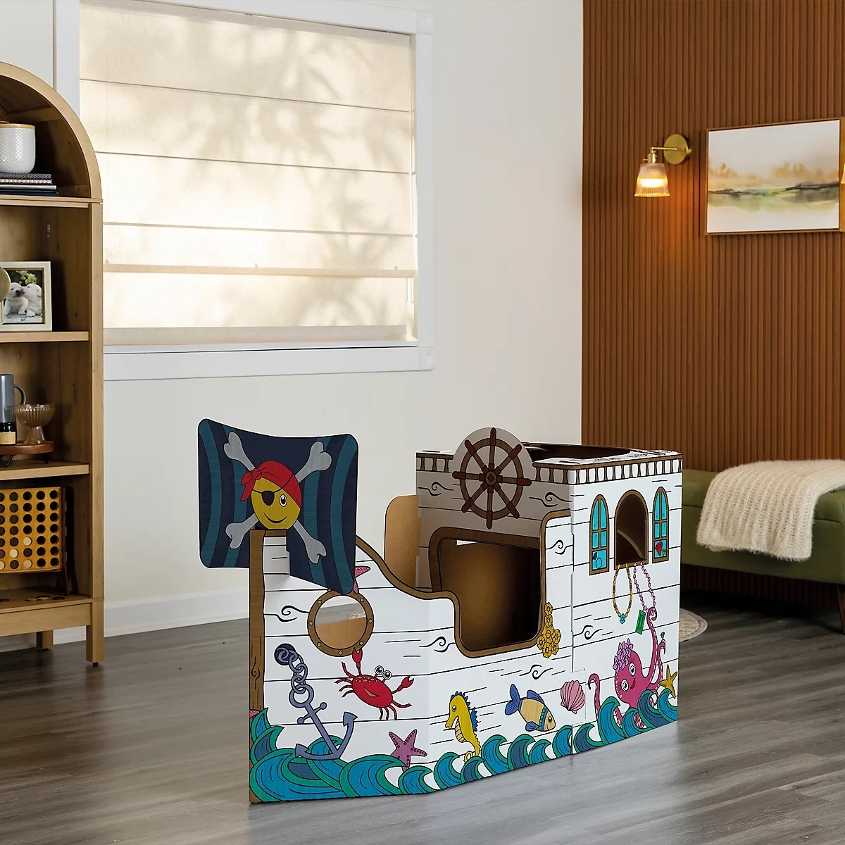 Ein Piratenschiff-Spielhaus aus Pappe mit einem Totenkopf am Mast. Es steht in einem Raum.