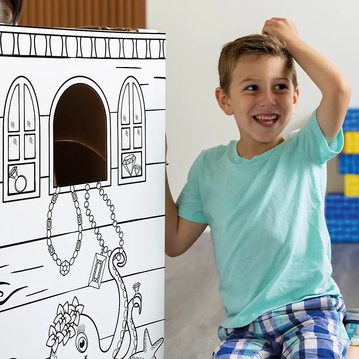 Ein lächelnder Junge steht neben einer schwarz-weißen, bemalten Piratenkiste mit Schmuck. Er hat eine Hand am Kopf.