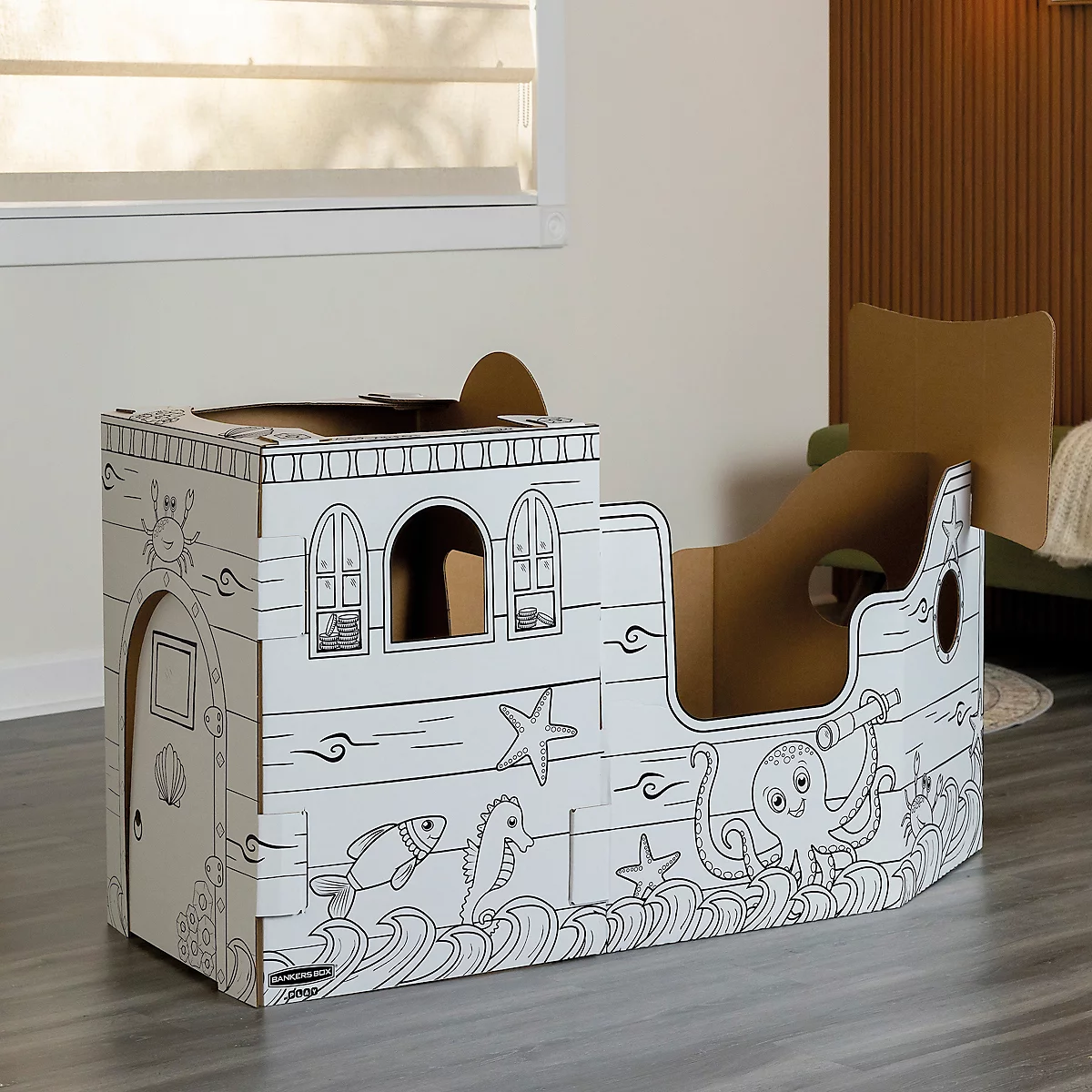 Un navire en carton, peint avec des créatures marines et des motifs maritimes. Les fenêtres et les portes sont également peintes.