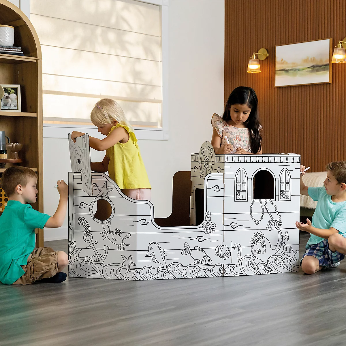 Kinderen kleuren een kartonnen schip in de woonkamer. Het schip is versierd met zeedieren. De kinderen zijn blij.