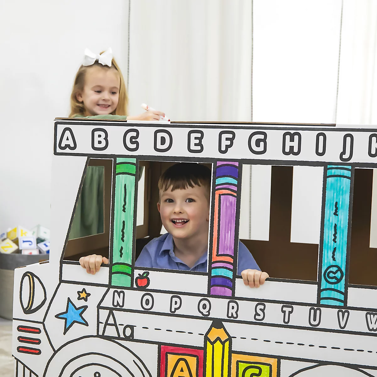Twee kinderen in een beschilderde kartonnen bus. Het meisje bovenaan draagt een strik, de jongen glimlacht.