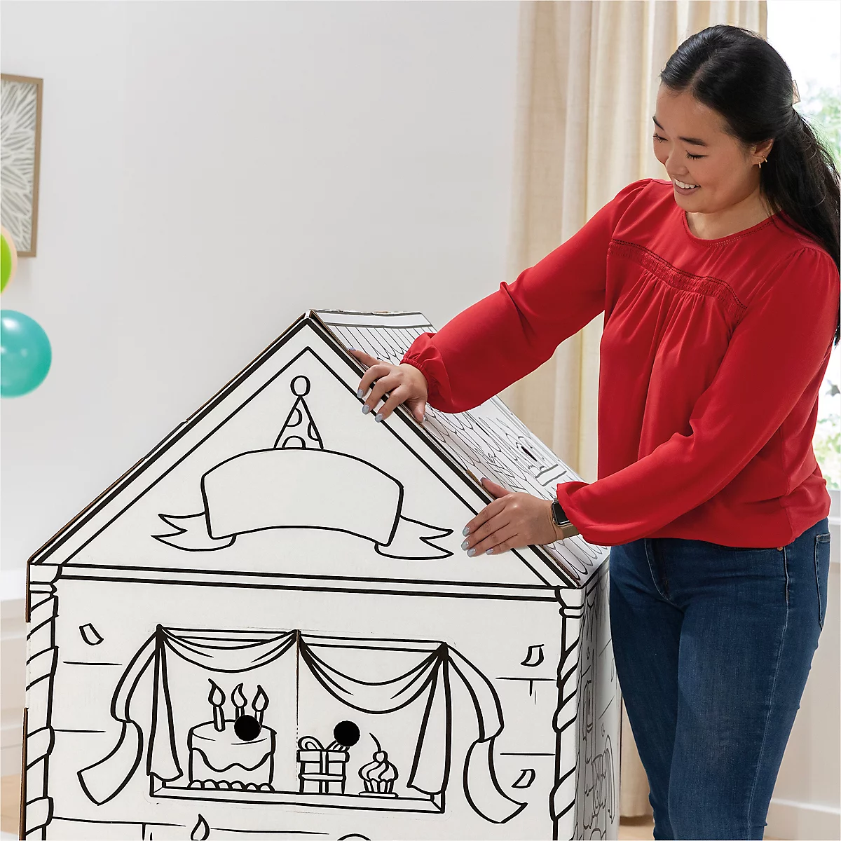 Een vrouw zet een kartonnen huis in elkaar met een verjaardagstaart en cadeaus erop.