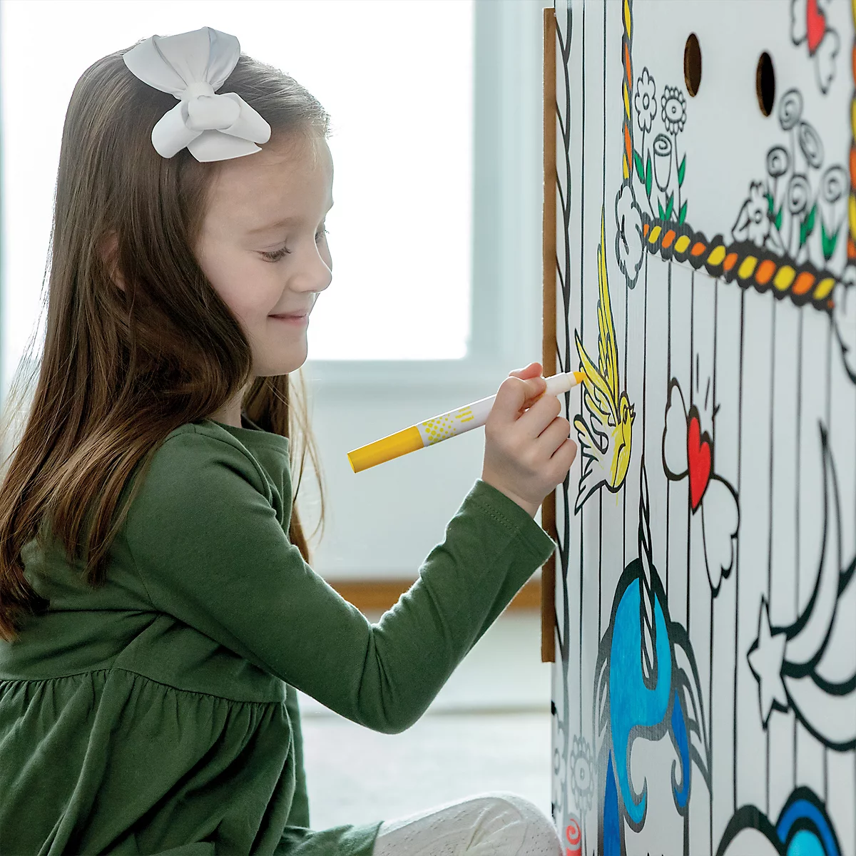 Ein lächelndes Mädchen malt mit einem gelben Stift einen Schmetterling auf eine Malwand.