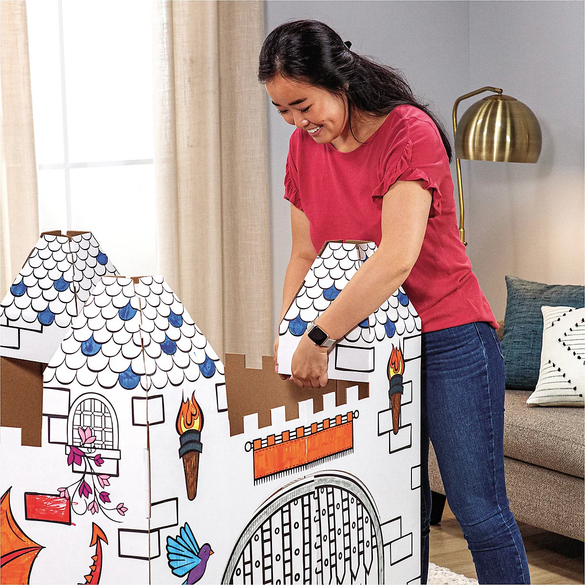 Une femme construit un château en carton, en ajoutant un toit. Le château est décoré de dessins colorés.