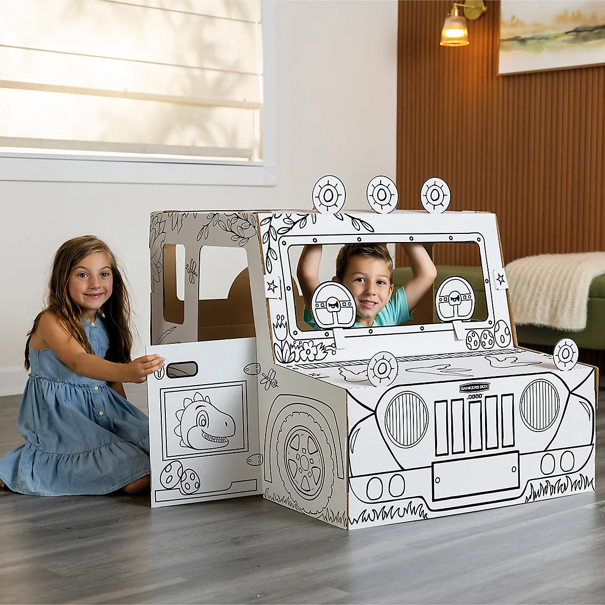 Deux enfants jouent dans une jeep en carton peinte. La fille ouvre la porte, le garçon regarde par la fenêtre.