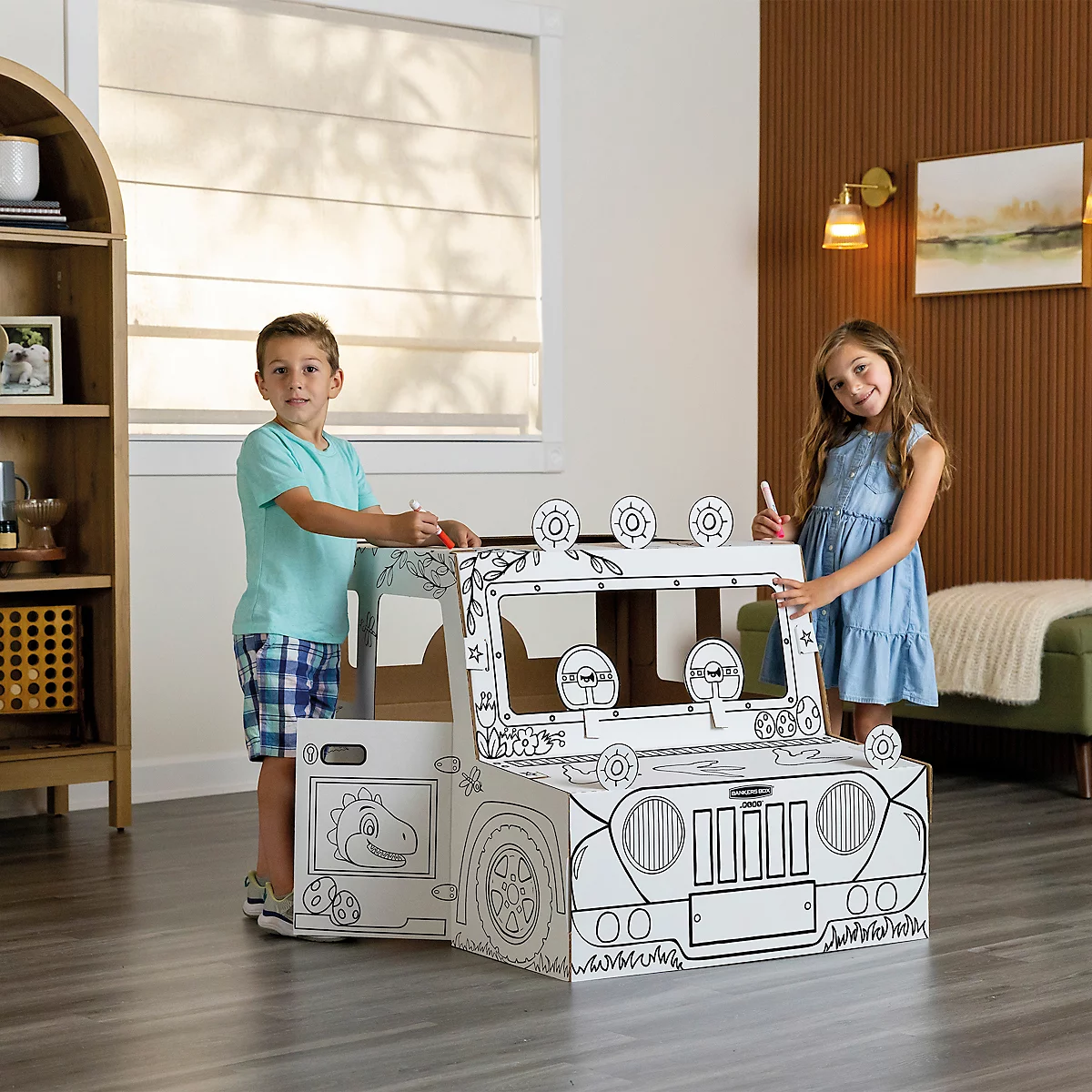 Twee kinderen kleuren een witte kartonnen jeep. Een jongen staat links, een meisje rechts.