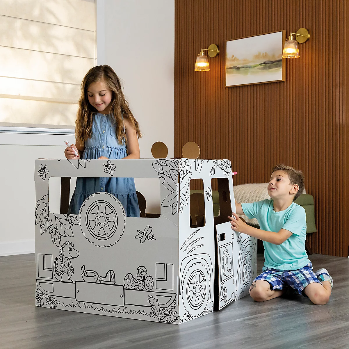 Zwei Kinder spielen mit einem bemalten Spielzeugauto aus Pappe. Das Mädchen steht im Auto, der Junge kniet daneben.