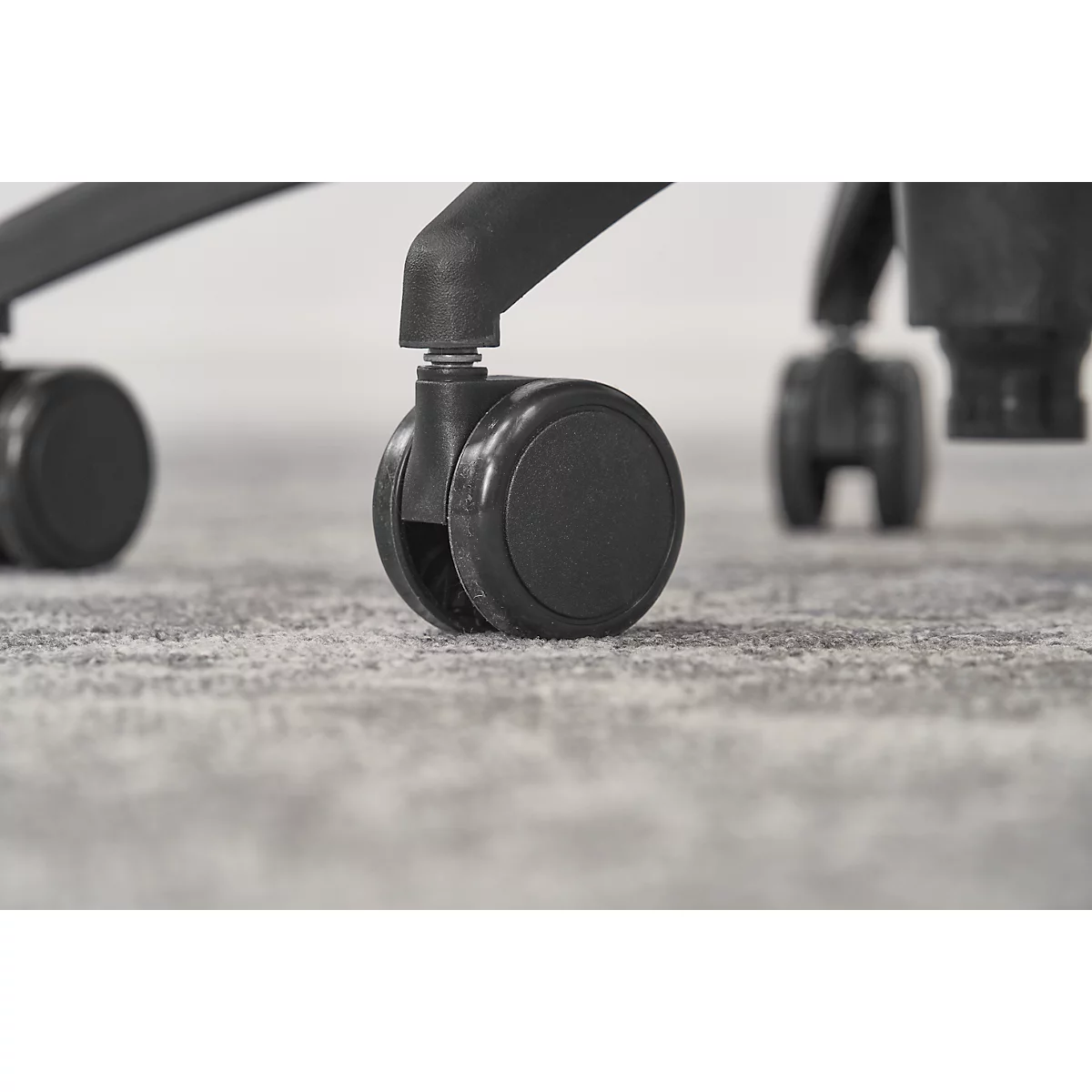 Close-up of black chair casters sitting on a gray textured carpet. Chair is partially in view.