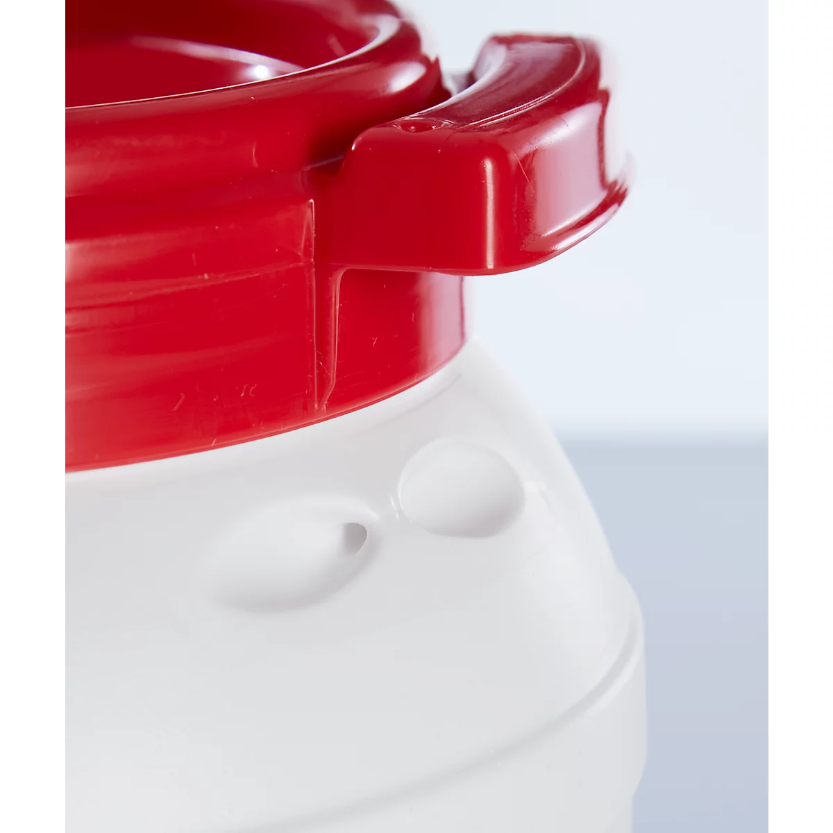 Gros plan d'une poignée rouge sur un récipient blanc, qui semble faire partie d'un produit plus grand.