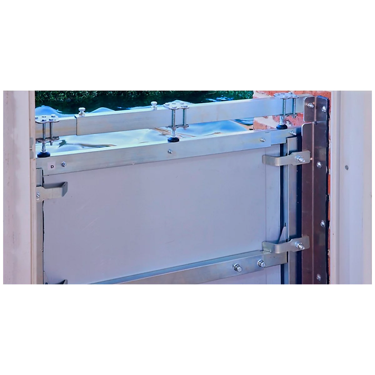 Gros plan d'une porte de protection contre les inondations argentée montée dans un cadre de porte. Des vis et des supports fixent la porte.