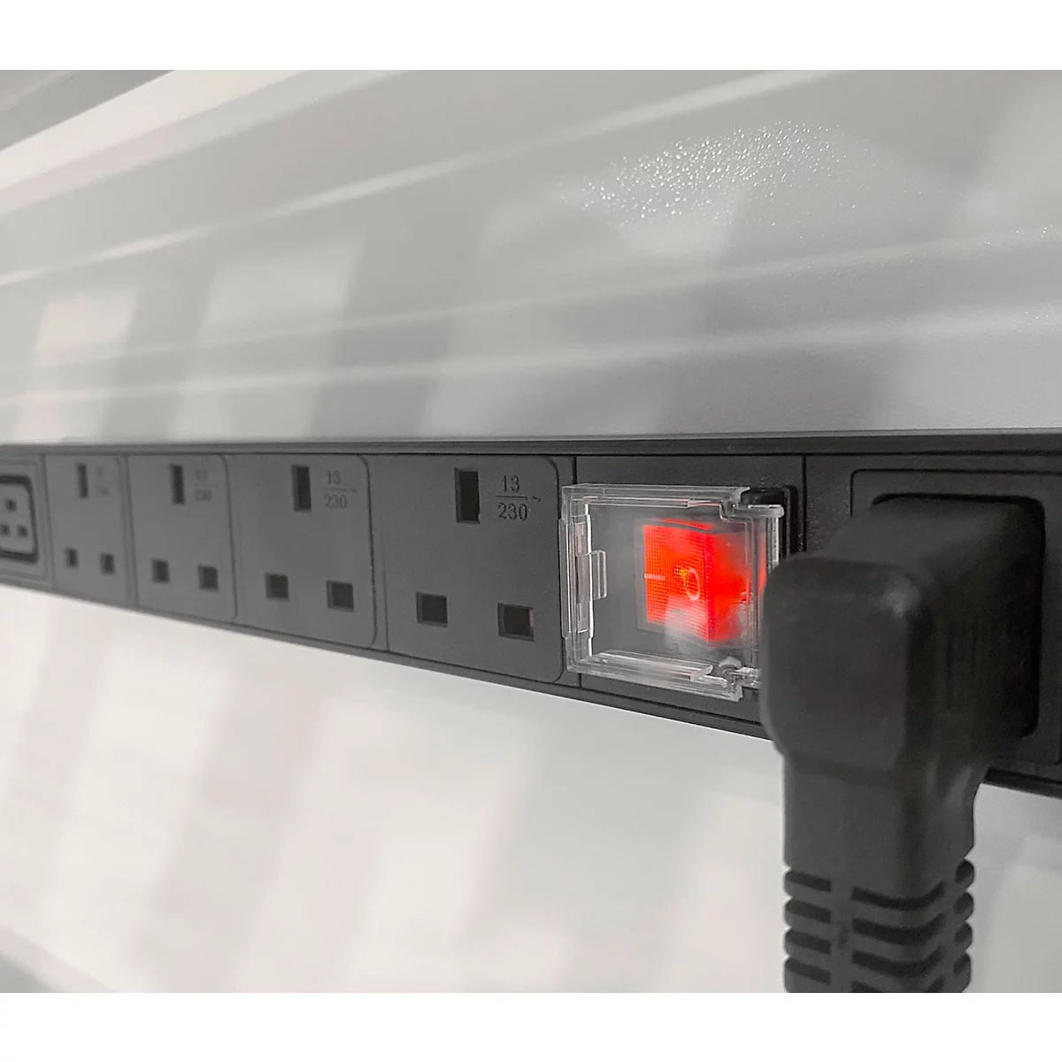 Graue Steckdosenleiste mit rotem Schalter und eingestecktem Stecker. Der Hintergrund ist weiß.