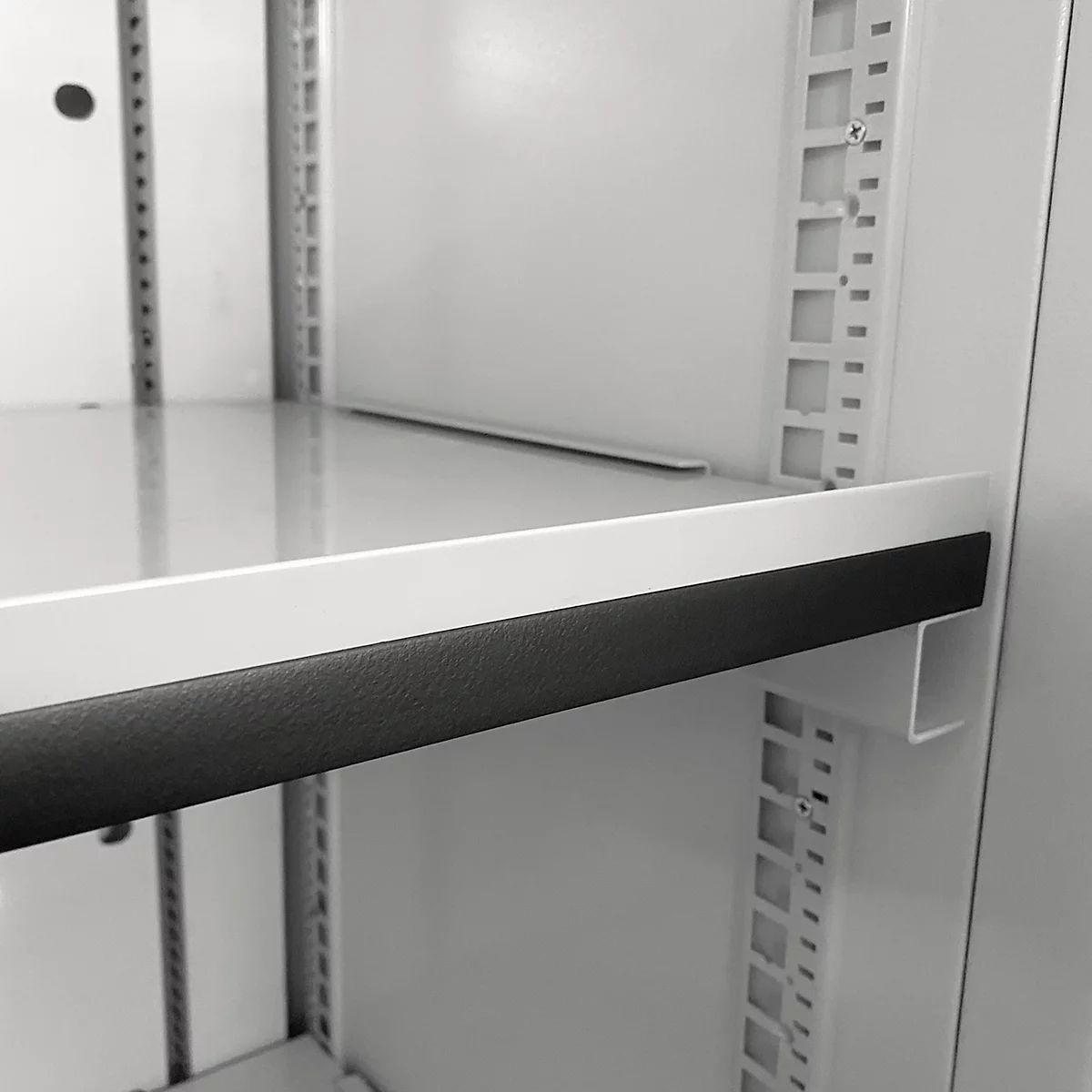 Nahaufnahme einer weißen Regalplatte mit schwarzem Kantenschutz in einem Metallschrank.