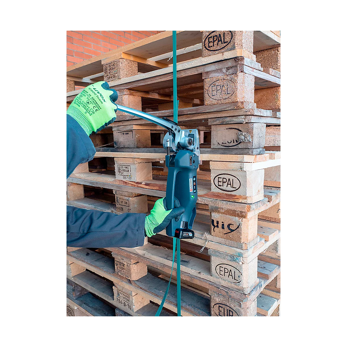 Persoon met groene handschoenen spant een band rond pallets met een blauw gereedschap. Op de achtergrond meer pallets.