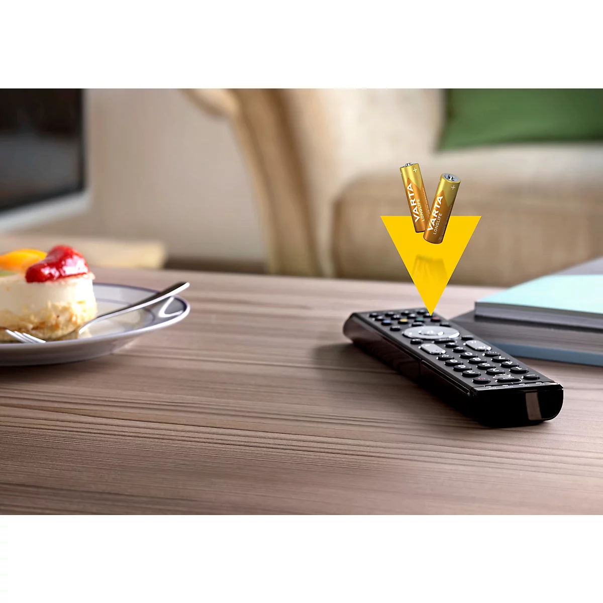 Remote control and batteries on a table. A piece of cake is next to it. Yellow arrow pointing to batteries.