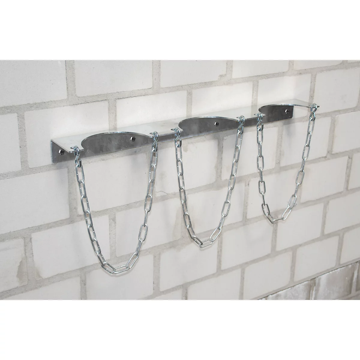 Silver gas bottle holder for three bottles, mounted on a white brick wall.