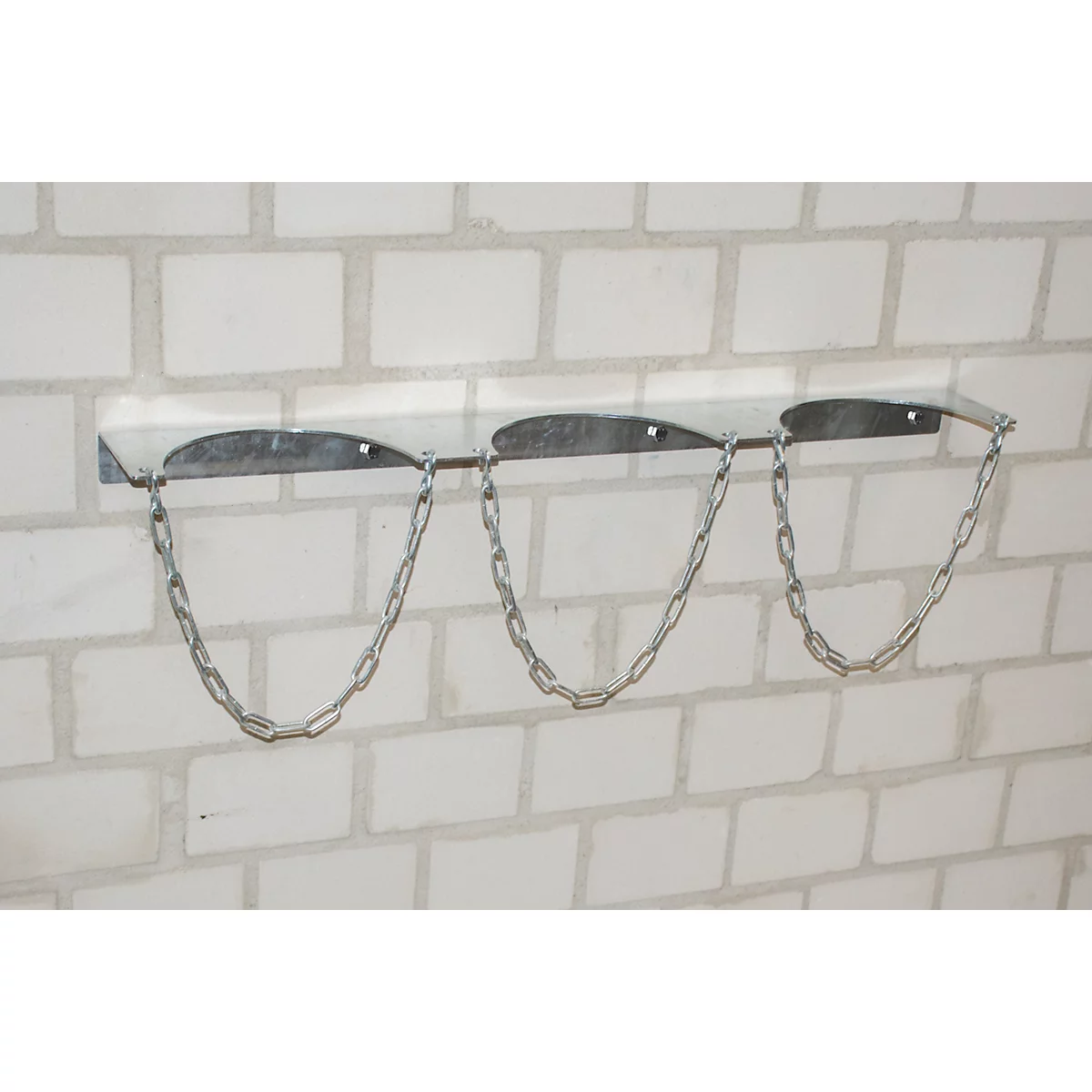 Gas bottle holder on white brick wall, three chains hanging down.