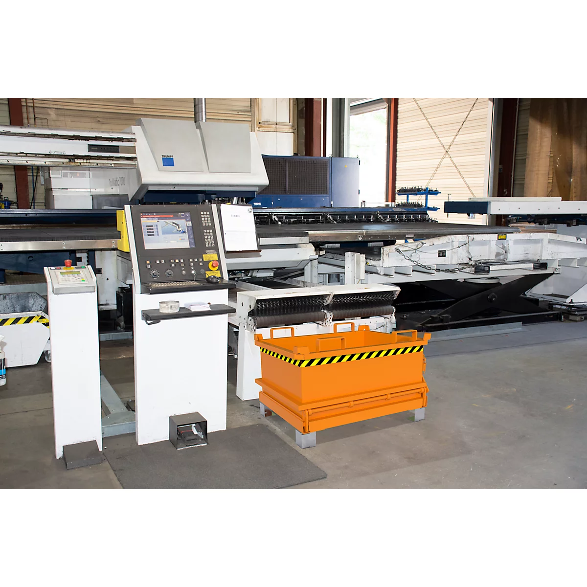 Industrielle Maschine mit Bildschirm und Bedienelementen. Orangefarbener Behälter mit schwarz-gelben Streifen. Fabrikumgebung.