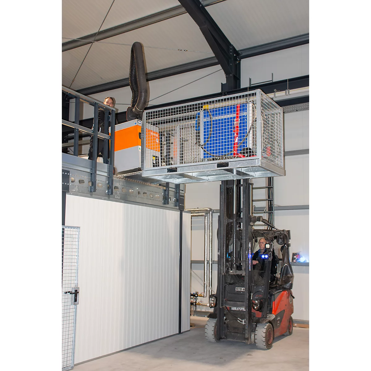Vorkheftruck die een machine in een fabriekshal optilt. Machine in metalen kooi, werknemer. Blauw, oranje.