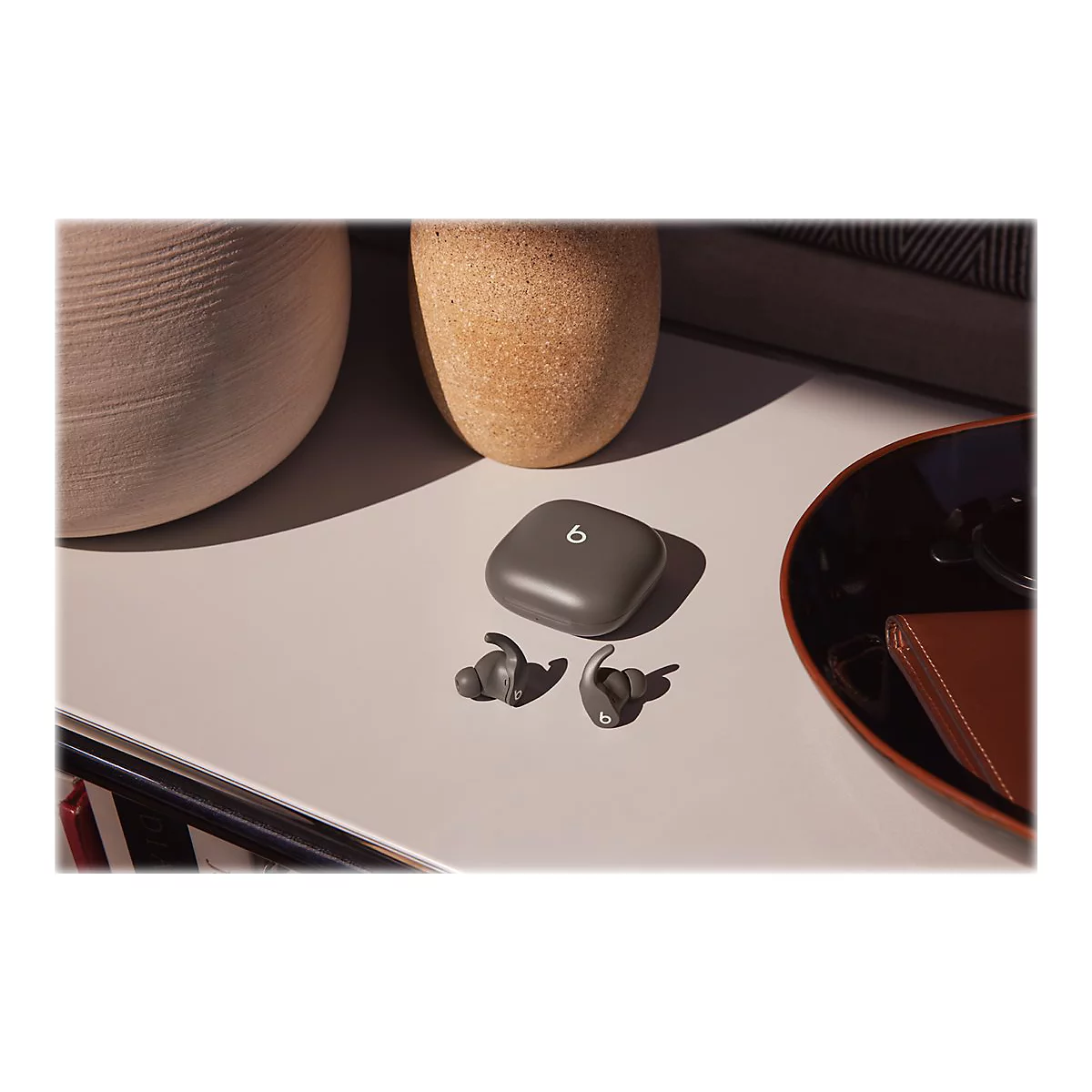 Drahtlose, graue In-Ear-KopfhÃ¶rer mit Ladecase auf weiÃŸem Tisch, im Hintergrund Vasen und Accessoires.