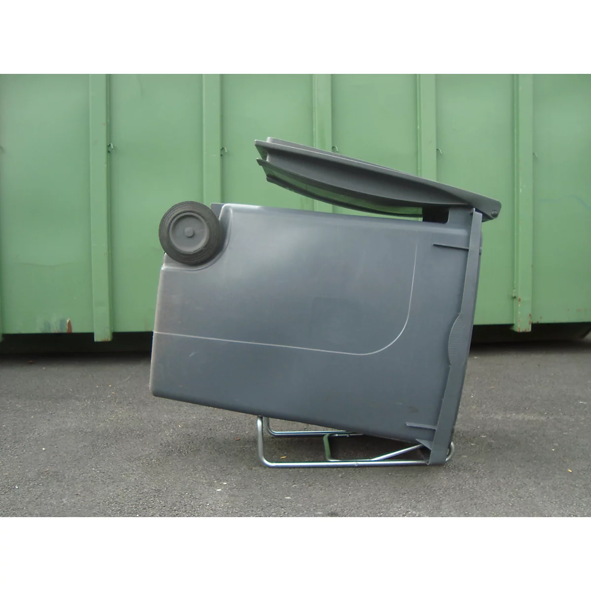 Graue Mülltonne mit offenem Deckel, steht auf einem Metallgestell. Im Hintergrund eine grüne Wand.