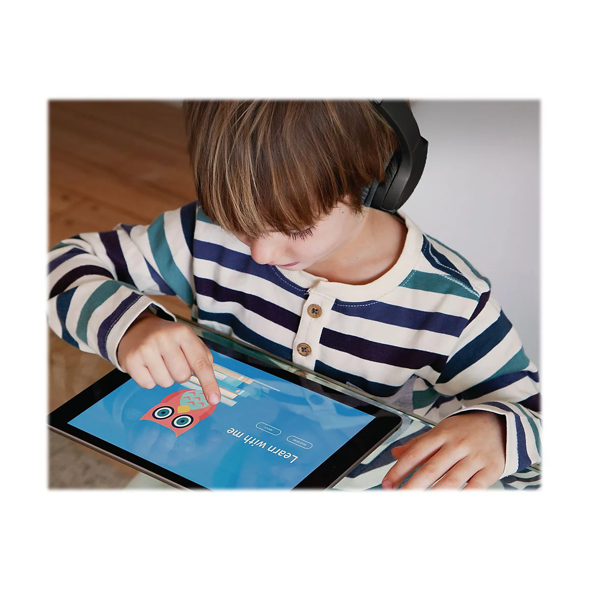 Enfant avec casque et tablette. Il touche l'Ã©cran. Sur la tablette, un motif de hibou avec le texte Learn with me.