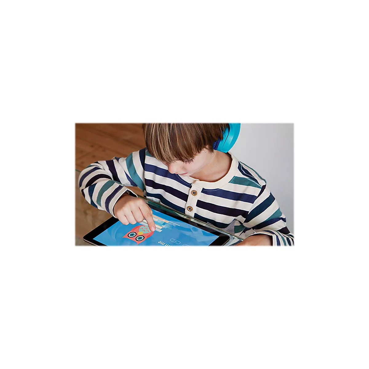 Ein Kind mit blauem Kopfhörer tippt auf einem Tablet, auf dem ein Eulen-Spiel angezeigt wird.