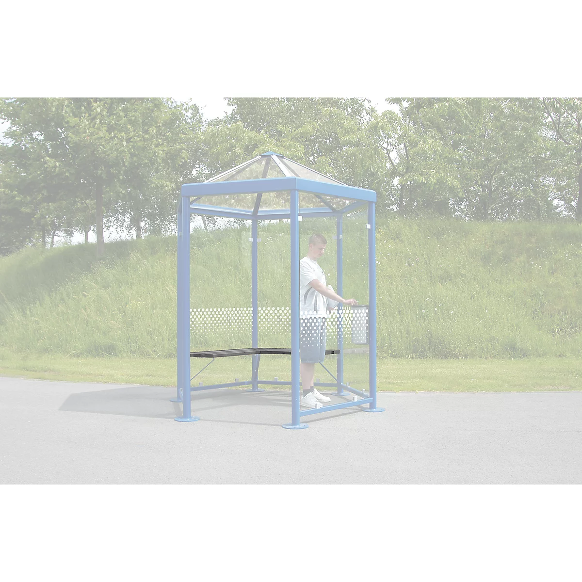 A man stands in a blue waiting shelter with a bench. Behind him is a meadow and trees.