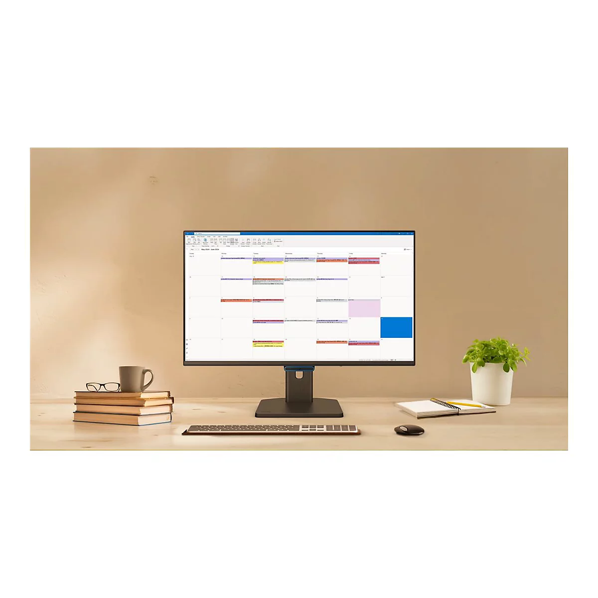 Ein Computermonitor auf einem Schreibtisch zeigt einen Kalender. Daneben stehen Bücher, eine Kaffeetasse und eine Pflanze.