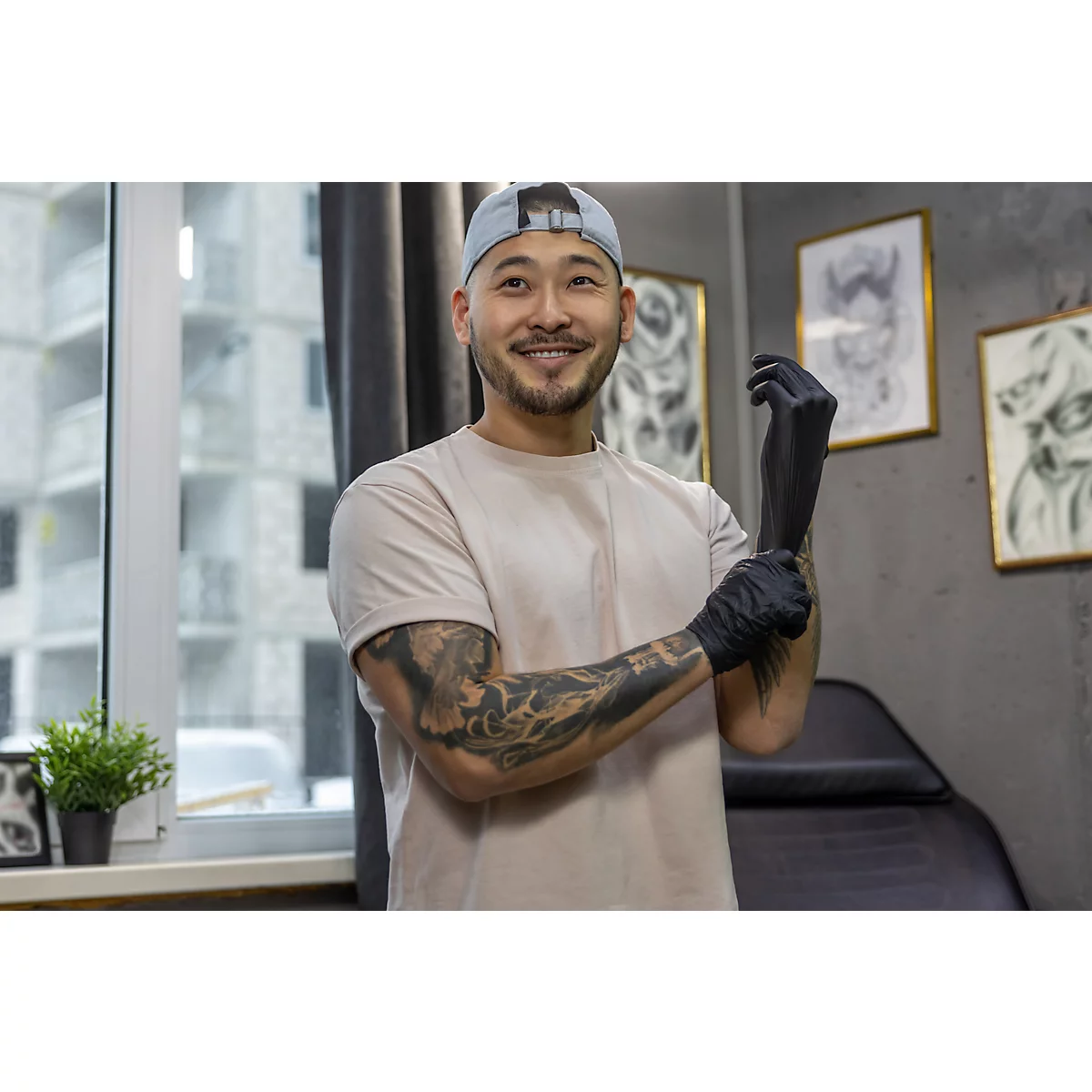 Een glimlachende tatoeëerder in een tattoo studio omgeving, die zwarte handschoenen aantrekt.