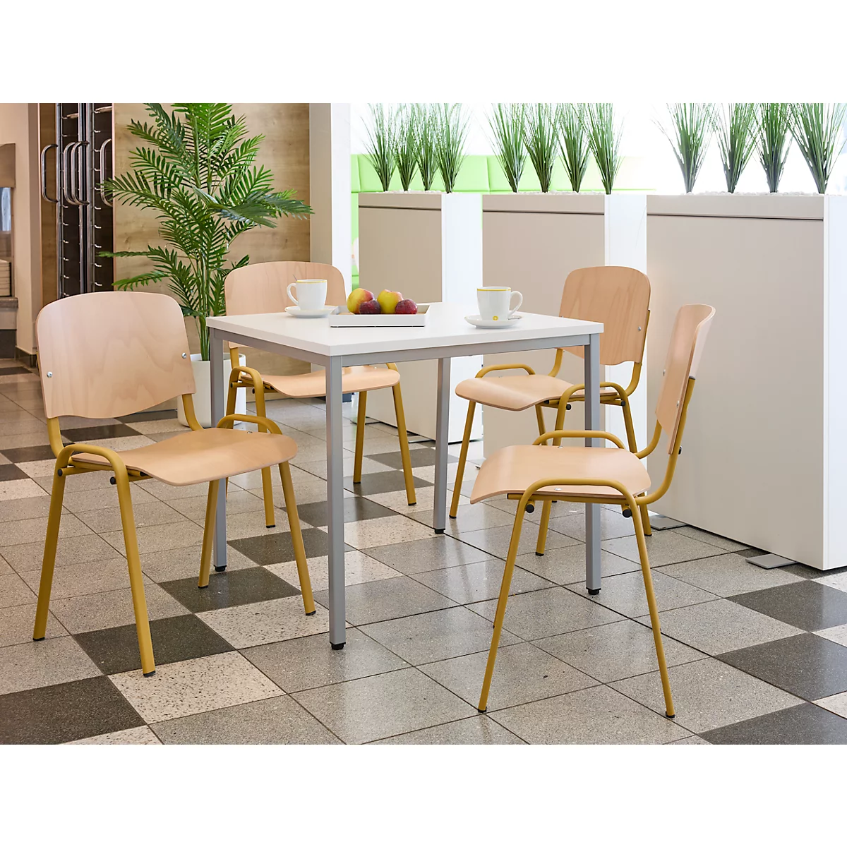 Essgruppe mit Tisch, Stühlen, Obst und Tassen. Helles Holz, gelbe Gestelle, Schachbrettmuster.