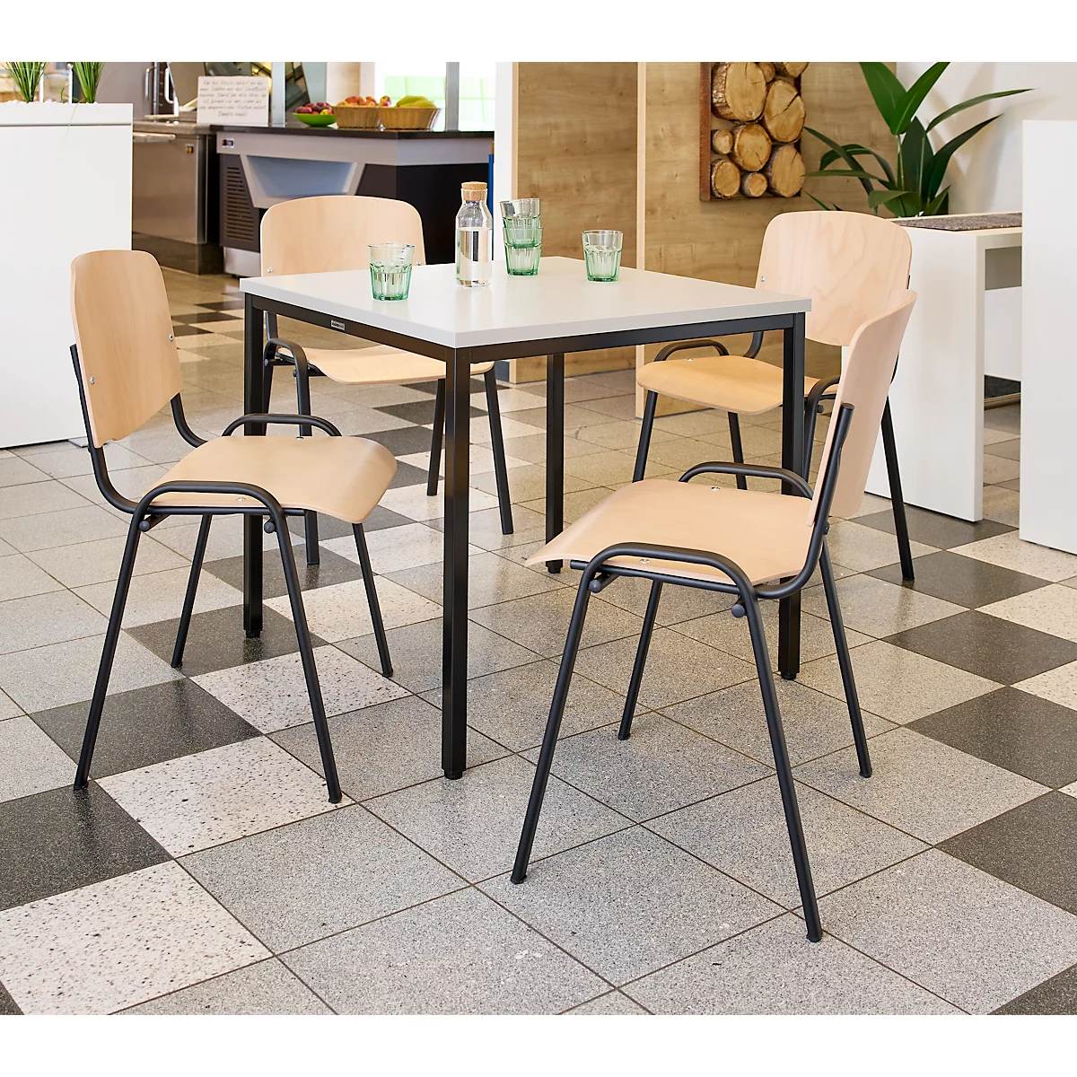 Essgruppe mit Tisch und Stühlen. Tischplatte weiß, schwarzes Gestell. Stühle Holz mit schwarzem Gestell. Auf dem Tisch Gläser und Wasserflasche.
